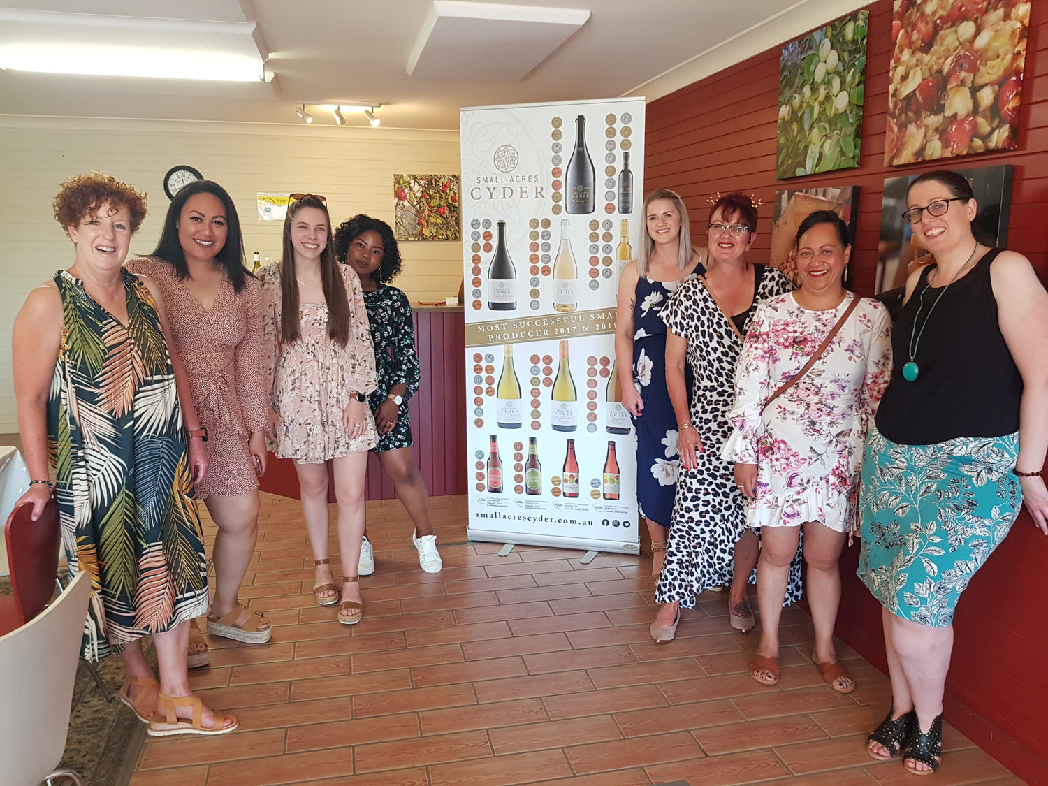 A group of women visiting the Small Acres Cyder tasting room in front of a banner featuring medals.