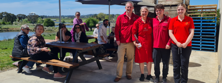 Four members of The Geoghegan Family dressed in red beside a group of people at picnic tables.